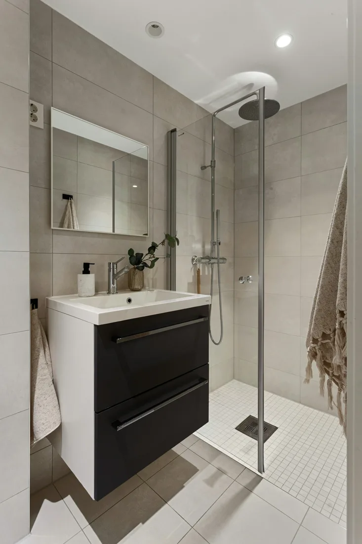 Compact tiled bathroom with a floating dark vanity, white sink top, and glass shower enclosure.