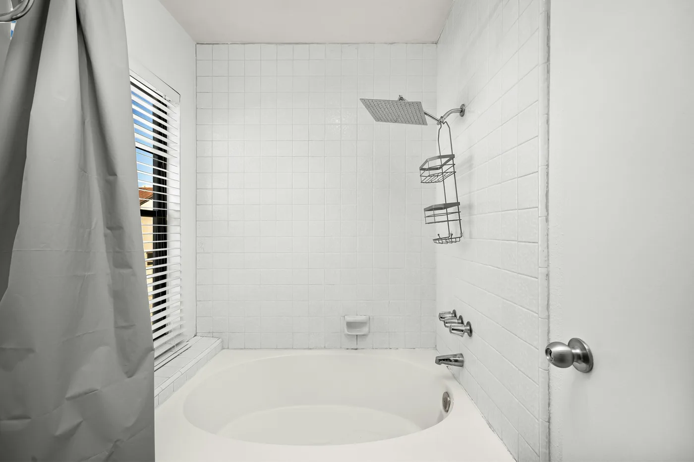 Existing white alcove bathtub with a tiled surround, window, curtain, and shower head.