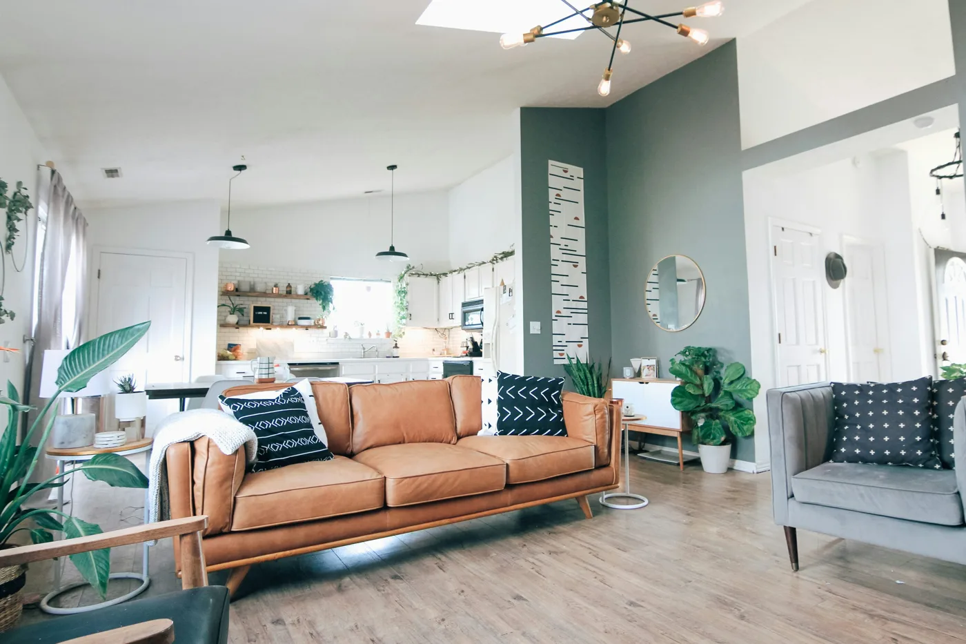 Bright open living room with wood-look flooring, a tan sofa and a kitchen beyond